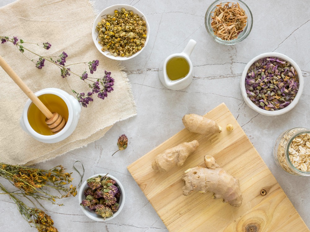 Herbs, ginger, honey, and oil on a marble surface, with dried flowers and oats.