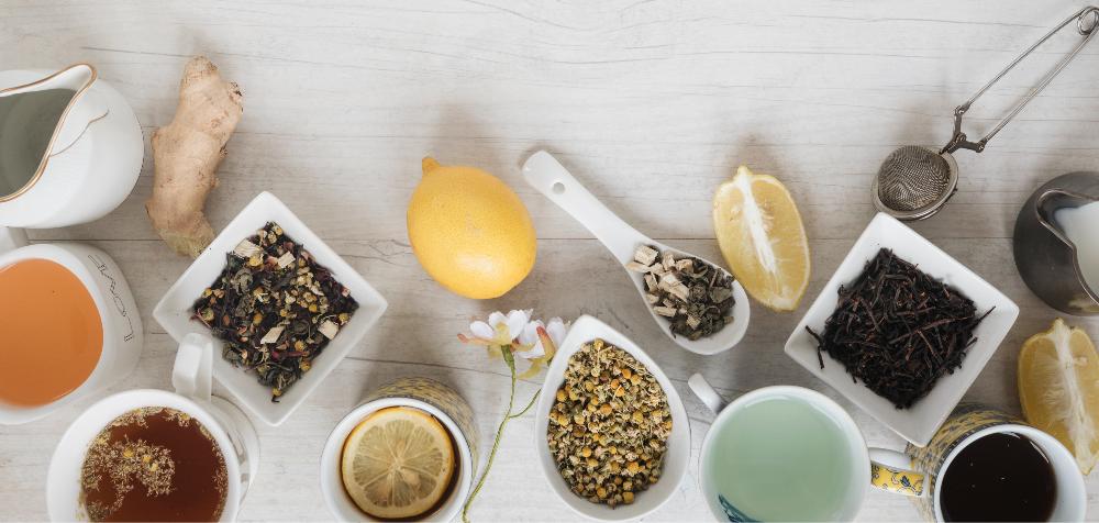 Assorted teas and ingredients, including lemon, ginger, and loose leaf tea, on a light surface.