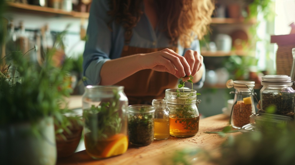 Woman preparing herbal tea with fresh herbs in a cozy kitchen.