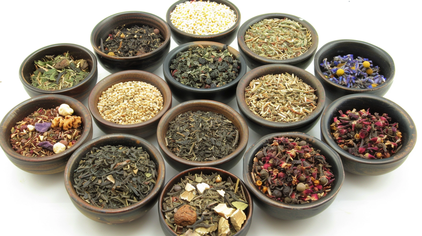 Assorted loose leaf teas and herbs in small bowls on a white background.